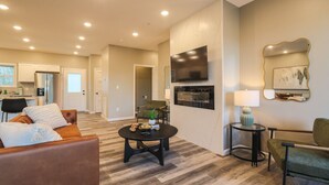 A modern living room with a fireplace, a flat-screen TV, and a dining area with a kitchen in the background. - 3BR Condo Near Ripken Experience & LeConte Center (Pigeon Forge)