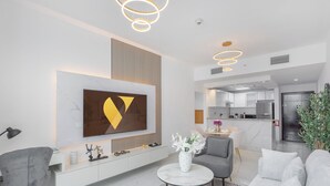 Un salon moderne avec un grand téléviseur, un canapé, une table basse et un coin repas, avec une cuisine en arrière-plan.