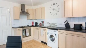 A modern kitchen with light wood cabinets, a built-in oven, a washing machine, and a clock on the wall.