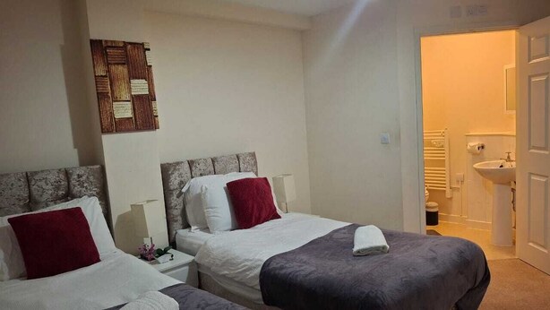 A hotel room with two beds, a decorative wall piece, a bathroom with a sink and toilet visible.