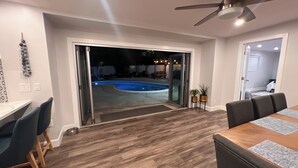 Un espace intérieur comprenant un coin repas, un ventilateur de plafond et donnant sur une piscine extérieure.