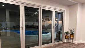 Un espace aménagé au bord de la piscine, avec une porte vitrée donnant sur un jardin.