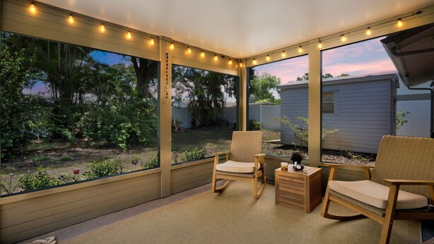 A covered patio with wicker chairs, a small table, and string lights.