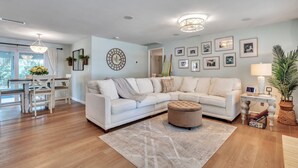 A spacious living room with a large L-shaped white sofa, a round coffee table, and a dining area with a white table and chairs.