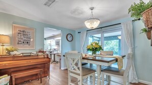 A dining area with a wooden table, white chairs, a chandelier, and a window with curtains.