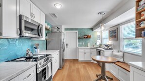 A modern kitchen with white cabinets, a stainless steel microwave, and a wooden dining table.
