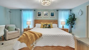 A bedroom with a bed, bedside tables, a chair, a lamp, a clock, and framed pictures on the wall.