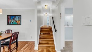 Una escalera de madera conduce a un segundo piso, un comedor con mesa y sillas, y un aplique en la pared.