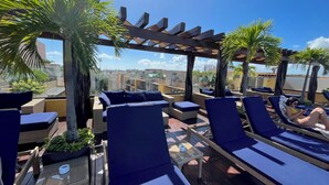 Un área de lounge en la azotea con sillones azules, una pérgola y palmeras.