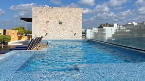 Una piscina en la azotea con agua azul cristalina, un muro de piedra y sillones de descanso.
