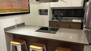Una cocina moderna con una isla central, taburetes de bar, un microondas y un refrigerador de acero inoxidable.