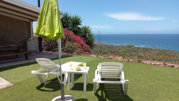 Un patio con césped artificial, una mesa con sillas y un paraguas verde.