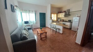Un espacio habitable compacto con sofá, una pequeña mesa de comedor, una zona de cocina con microondas y estufa, y un televisor en una esquina.