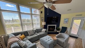 A living room with a sectional sofa, two armchairs, a patterned ottoman, and a ceiling fan. - 7BR Walk-to-Beach Corolla Home • Hot Tub • Family-Friendly • Sleeps 16+ (Corrolla)