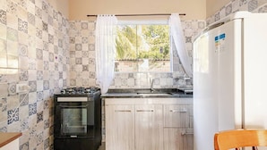 A compact kitchen with a gas stove, oven, and a white refrigerator. - Casa Ilha de Sol (Ilhabela)