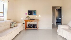 A modern living room with a sofa, a coffee table with speakers, a flat-screen TV, and a small plant. - Casa Ilha de Sol (Ilhabela)