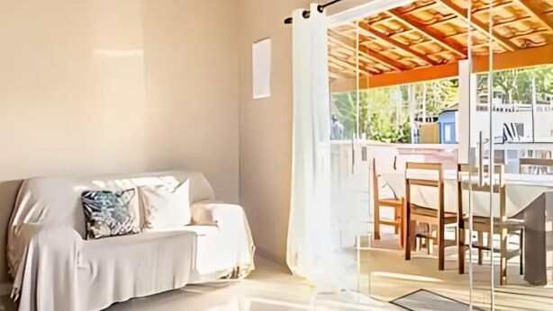 A modern hotel room with a glass door leading to an outdoor area, a sofa with cushions, and a wooden ceiling structure. - Casa Ilha de Sol (Ilhabela)