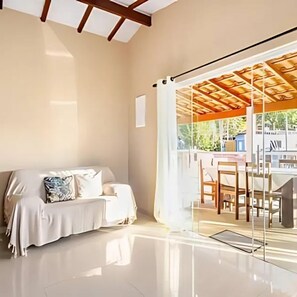 A modern hotel room with a glass door leading to an outdoor area, a sofa with cushions, and a wooden ceiling structure. - Casa Ilha de Sol (Ilhabela)