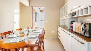 A compact kitchen with a dining area, featuring a microwave, cabinets, and a dining table set for four. - Casa Ilha de Sol (Ilhabela)