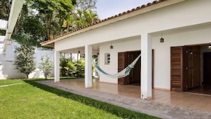 Un espacio exterior techado con una hamaca, paredes blancas y piso de baldosas.