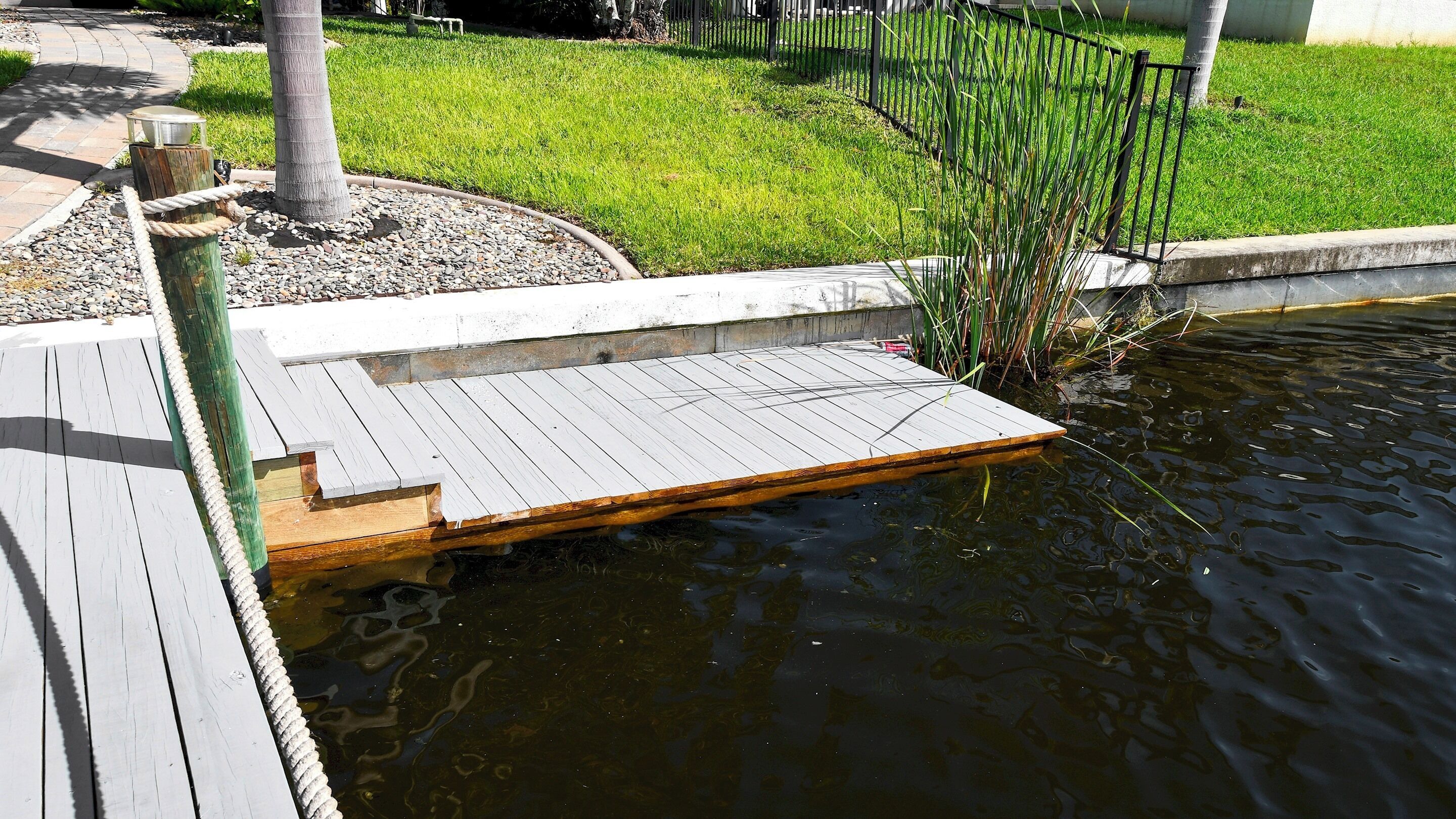 A wooden deck extending over a pond with a grassy area and a fence in the background.