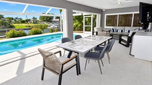 A modern outdoor dining area with a pool view, a ceiling fan, and a flat-screen TV.