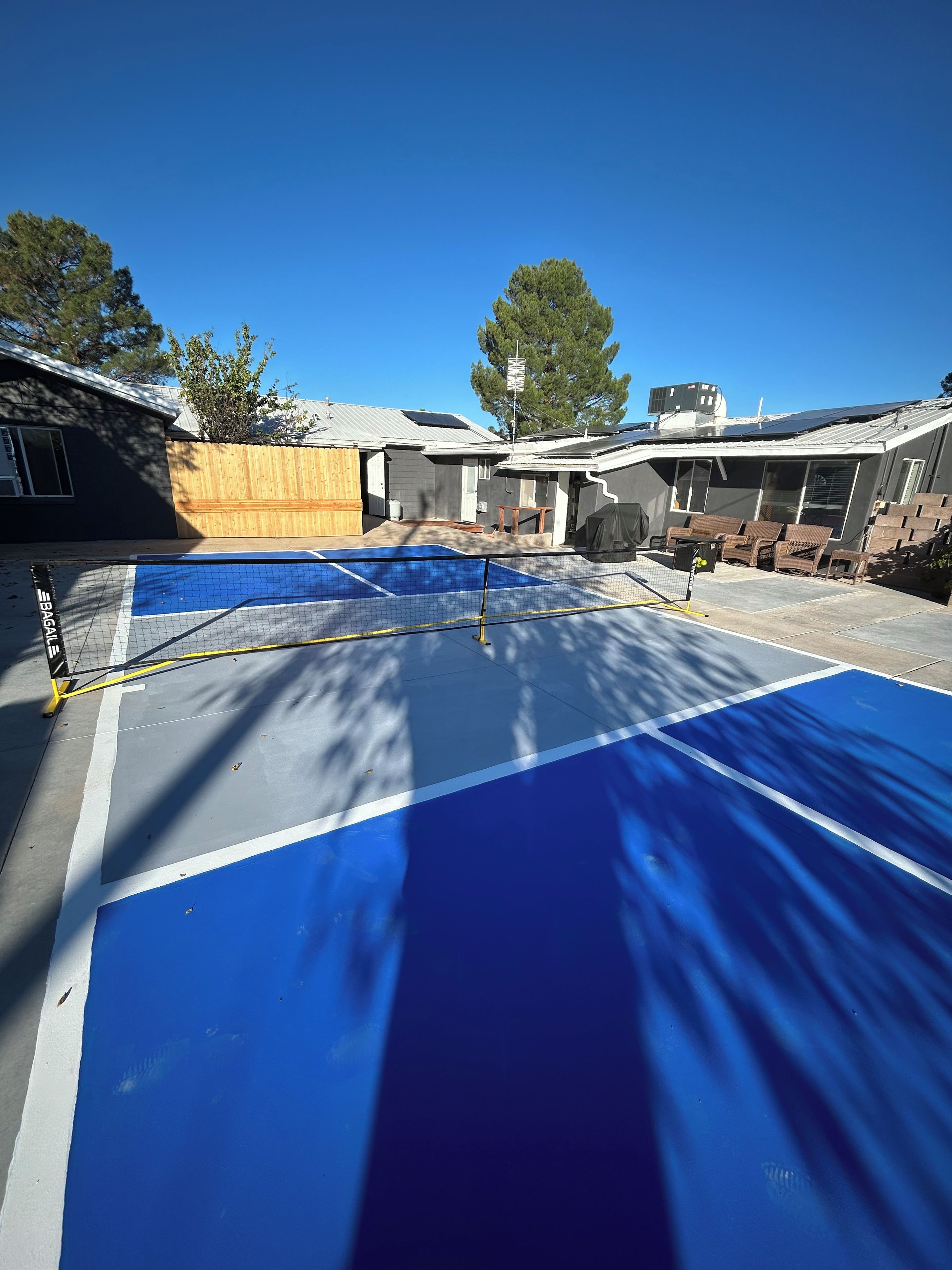 A residential area with a blue tennis court, a wooden fence, and a house with solar panels.