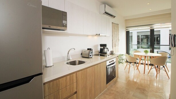 A modern kitchen with a built-in microwave, toaster, and coffee maker. There is a sink, a dishwasher, and a dining area with a table and chairs. - Ipana by The Spot Rentals (Playa del Carmen)