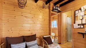 A wooden cabin interior with a sofa, wicker chairs, a hanging light fixture, and a wall with notes and pictures. - Cabin 'Pátio do Pescador' with Private Terrace, Private Garden, and Wi-Fi (Peniche)