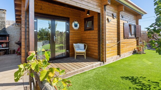 A wooden cabin with a deck, a sliding glass door, and a chair outside. - Cabin 'Pátio do Pescador' with Private Terrace, Private Garden, and Wi-Fi (Peniche)