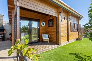A wooden cabin with a deck, a sliding glass door, and a chair outside. - Cabin 'Pátio do Pescador' with Private Terrace, Private Garden, and Wi-Fi (Peniche)