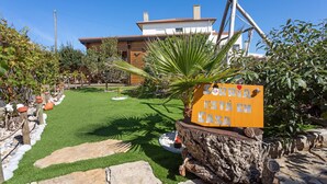 A well-maintained garden with a sign, a wooden structure, and a building in the background. - Cabin 'Pátio do Pescador' with Private Terrace, Private Garden, and Wi-Fi (Peniche)