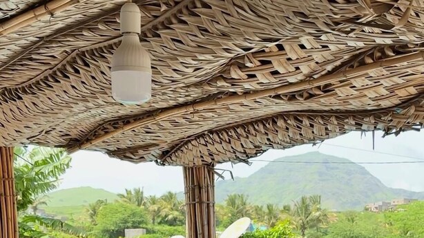 A couple toasting with a drink at a wooden table under a thatched roof, overlooking a pool and lush greenery. - Quinta Refúgio (São Domingos)