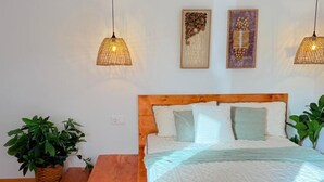 A bedroom with a wooden headboard, two wall-mounted lamps, a bed with white bedding, and two potted plants. - Quinta Refúgio (São Domingos)