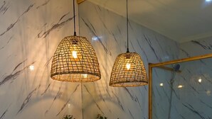 A bathroom with a marble wall, wooden vanity, two pendant lights, a mirror, and a shower. - Quinta Refúgio (São Domingos)
