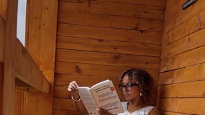 A person sitting on a wooden chair in a wooden cabin reading a book. - Quinta Refúgio (São Domingos)