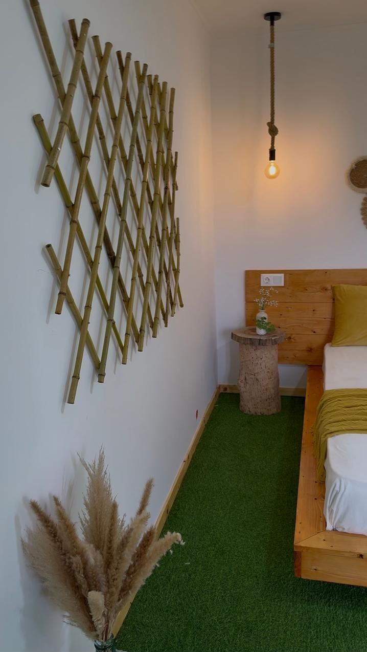 Una habitación con cabecera de madera, una mesita redonda con un florero, una lámpara de pared y un adorno de bambú en la pared.