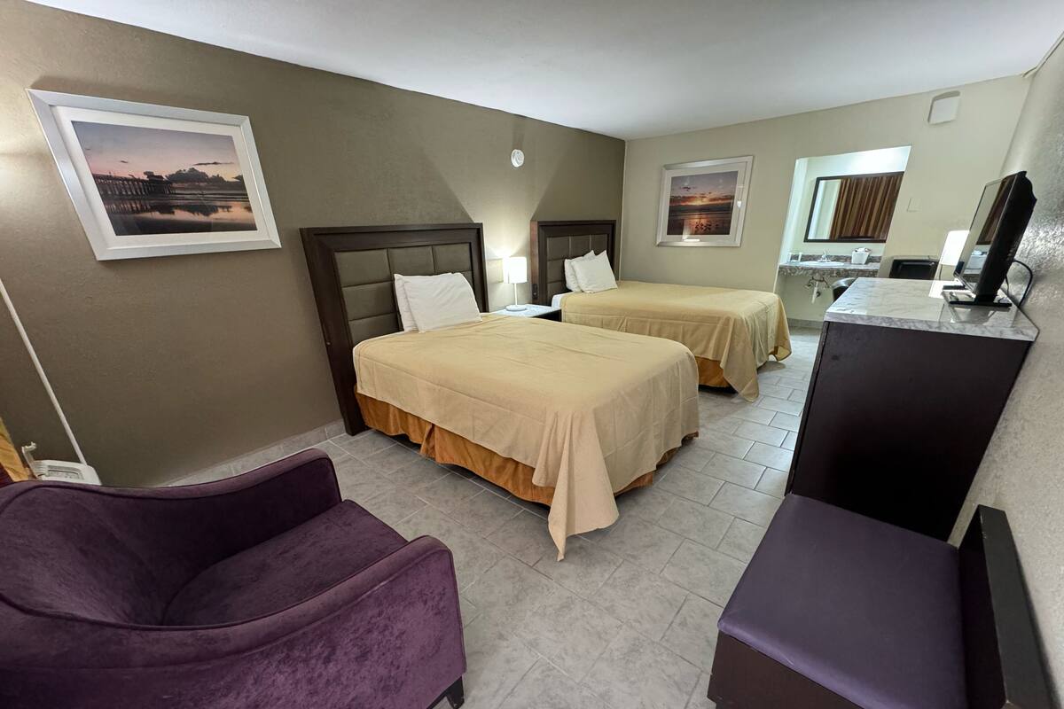 A hotel room with two beds, a desk, a chair, and a TV.