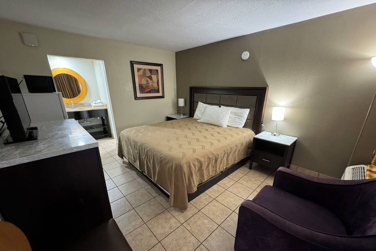 A hotel room with a bed, a desk, a chair, and a bathroom.