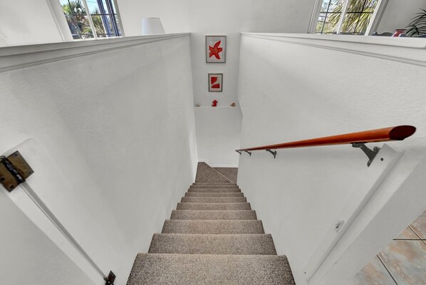 A carpeted staircase with a wooden handrail, white walls, and two red wall decorations. - Classic Surf Lodge with Beach Supplies, Walk to Beach & Marina, Near IMG Academy (Cortez)