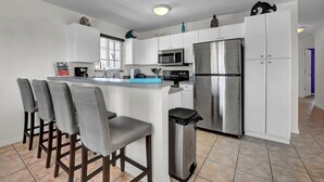 A modern kitchen with white cabinets, stainless steel appliances, and a bar area with four stools.