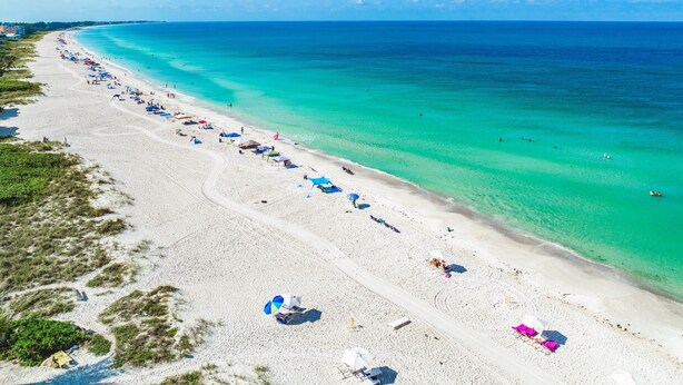 A wide beach with clear turquoise waters and a long stretch of beach umbrellas and sun loungers.