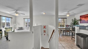 A spacious living area with a high ceiling, large windows, a dining area, and a kitchen.