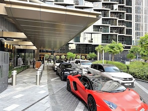 A modern building with a covered entrance, parked luxury cars, and a well-maintained outdoor area with greenery.
