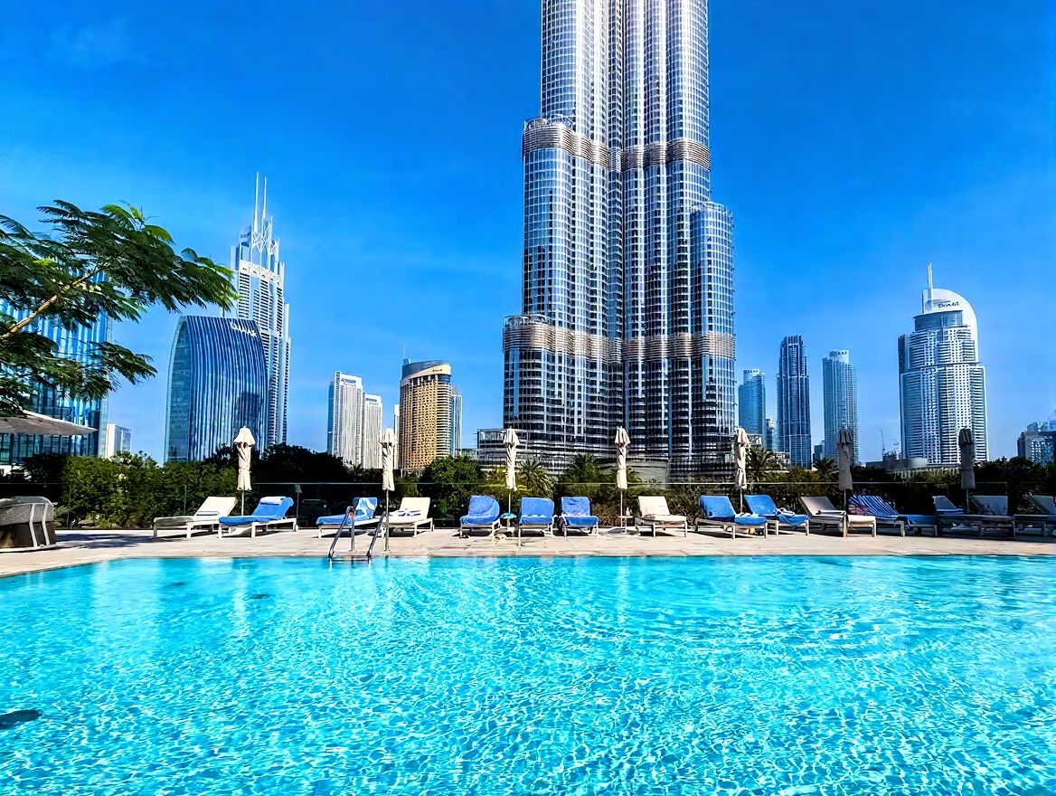 A swimming pool with lounge chairs and a city skyline in the background.