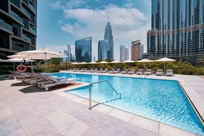 Ein Pool auf dem Dach mit Liegestühlen und Sonnenschirmen, umgeben von Hochhäusern.