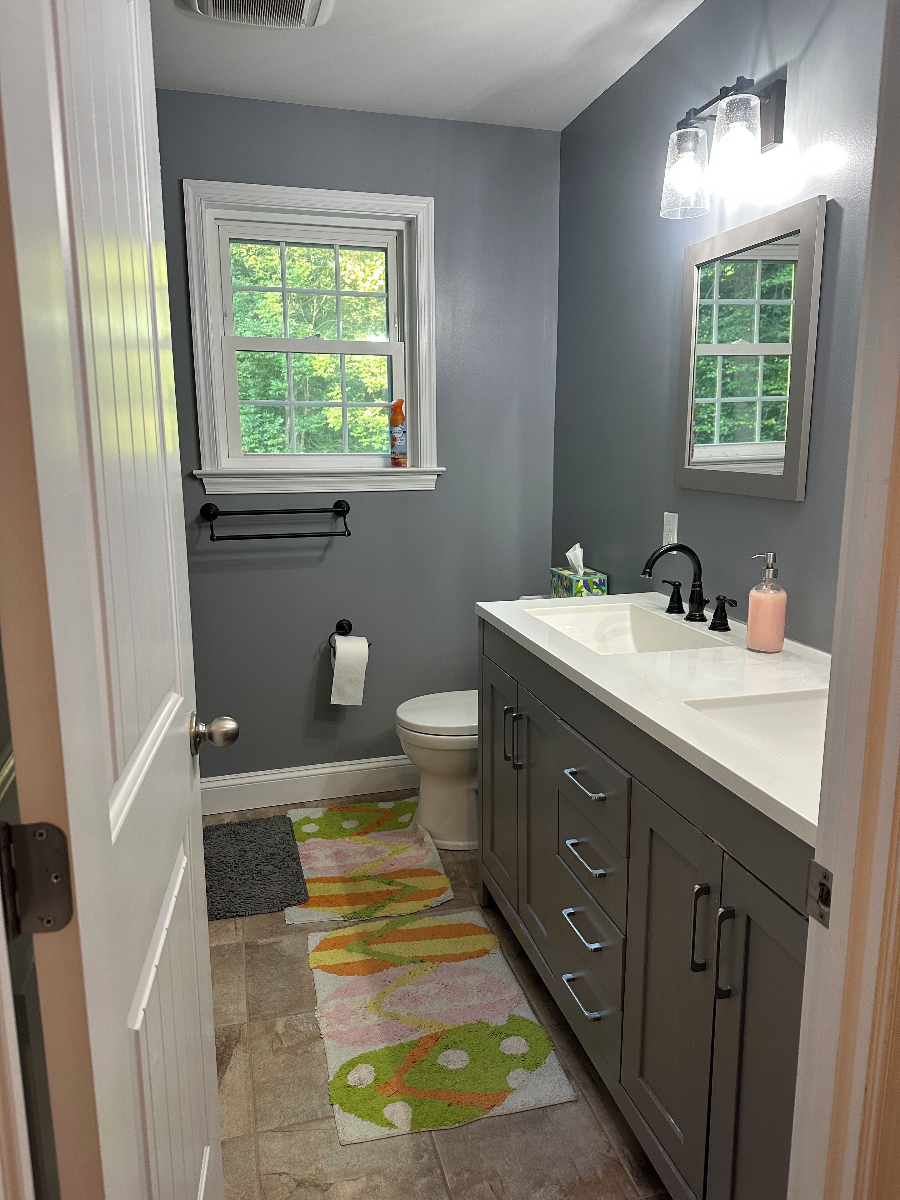 A bathroom with a white sink, dark gray cabinets, a toilet, and a window with a view of trees.