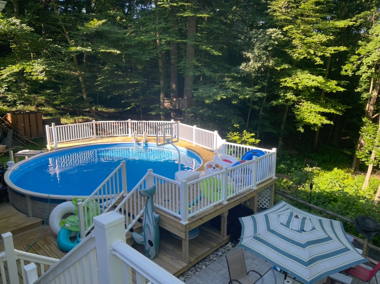 A backyard with a swimming pool, wooden deck, and a covered seating area.