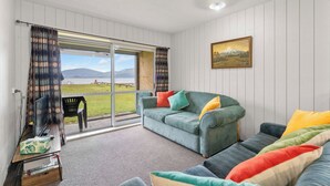Un salon confortable avec un canapé, un téléviseur et une vue sur un lac et des montagnes, grâce à de grandes fenêtres.