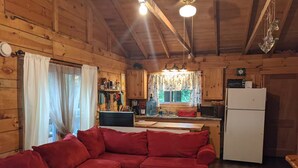 Een gezellig interieur van een chalet met een rode bank, houten wanden, een keuken met een koelkast en een raam met gordijnen.